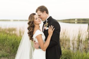 Happily Married Couple Embracing in Front of Waterfront View, Bride with Hair and Makeup by Kristy's Artistry Design Team