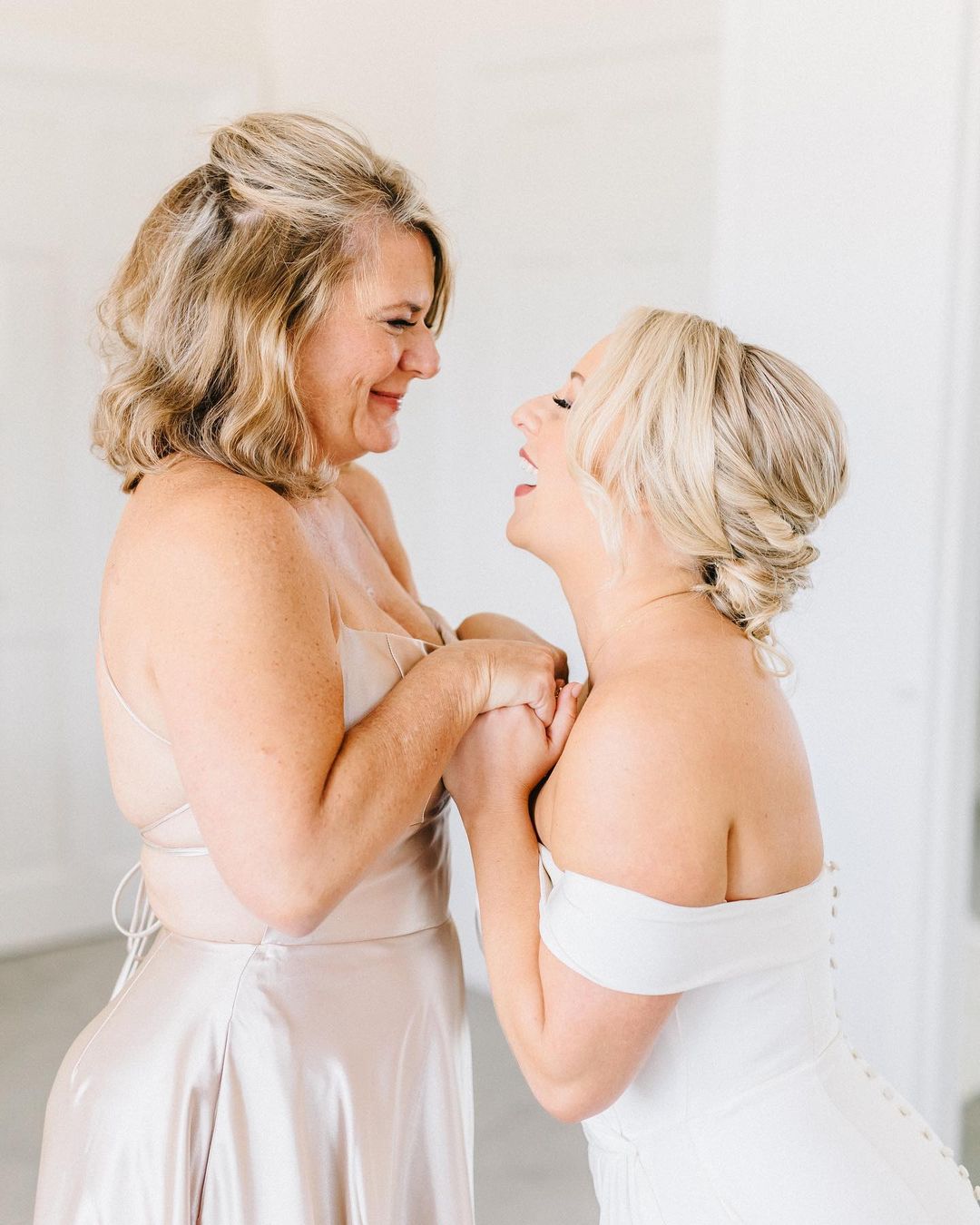 Mother of the bride and bride smiling, laughing, and holding hands with hair and makeup done by Kristys Artistry Design Team.
