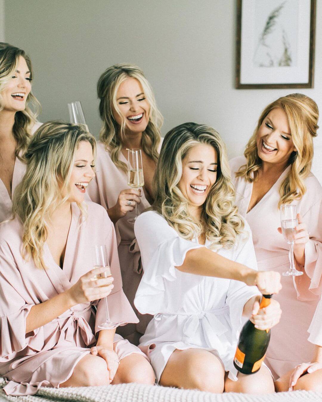 Bride and bridal party popping champagne and smiling with hair and makeup done by Kristy's Artistry Design Team.