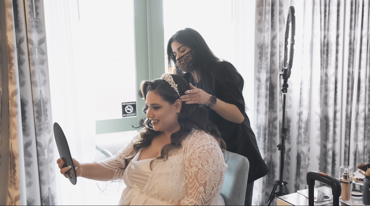 Hair stylist from Kristy's Artistry Design Team applying the finishing touches to a bride's hair as the bride looks over her work.