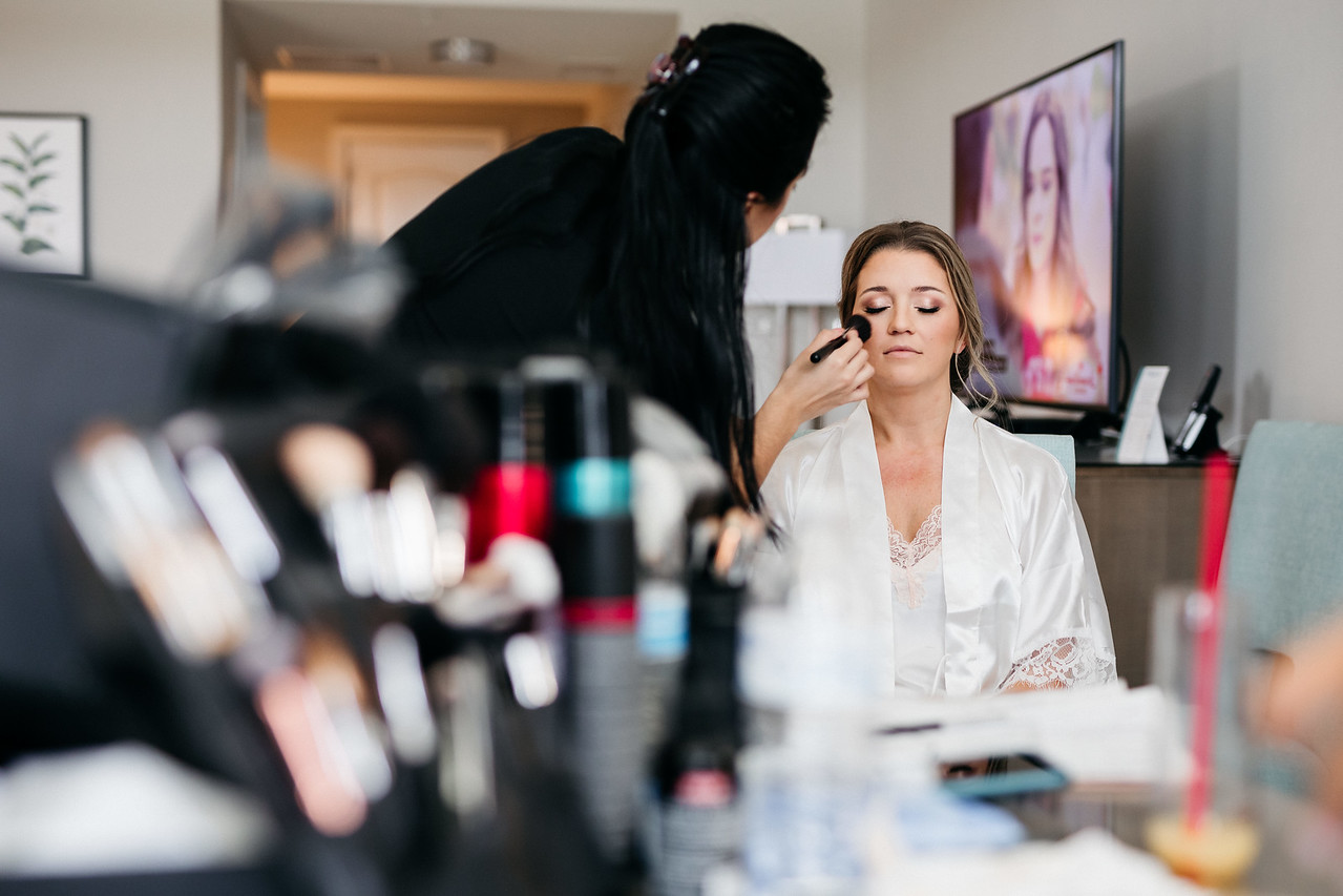 Makeup artist from Kristy's Artistry Design Team applying makeup to a bride in her hotel room, showcasing their mobile hair and makeup services.