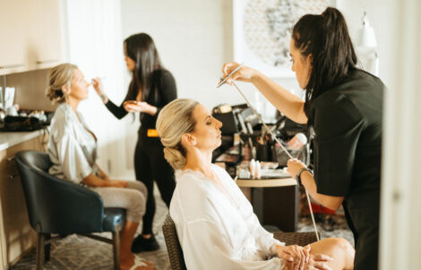 Two makeup artists applying airbrush makeup to different members of the bridal party, showcasing their teamwork and expertise.