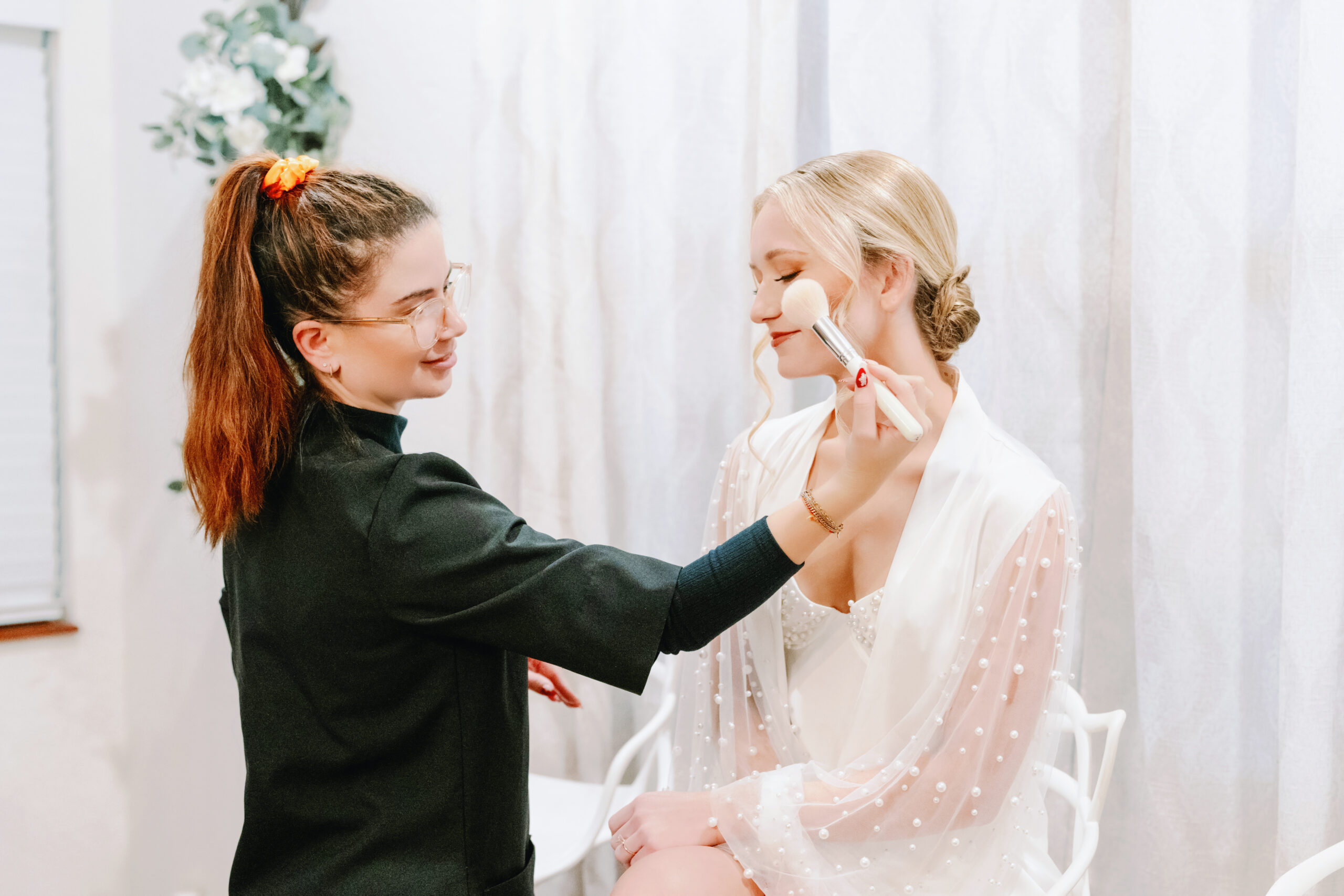 Makeup artist applying finishing touches to a bride in Orlando, FL, with her hair styled in a bun by Kristy's Artistry Design Team.