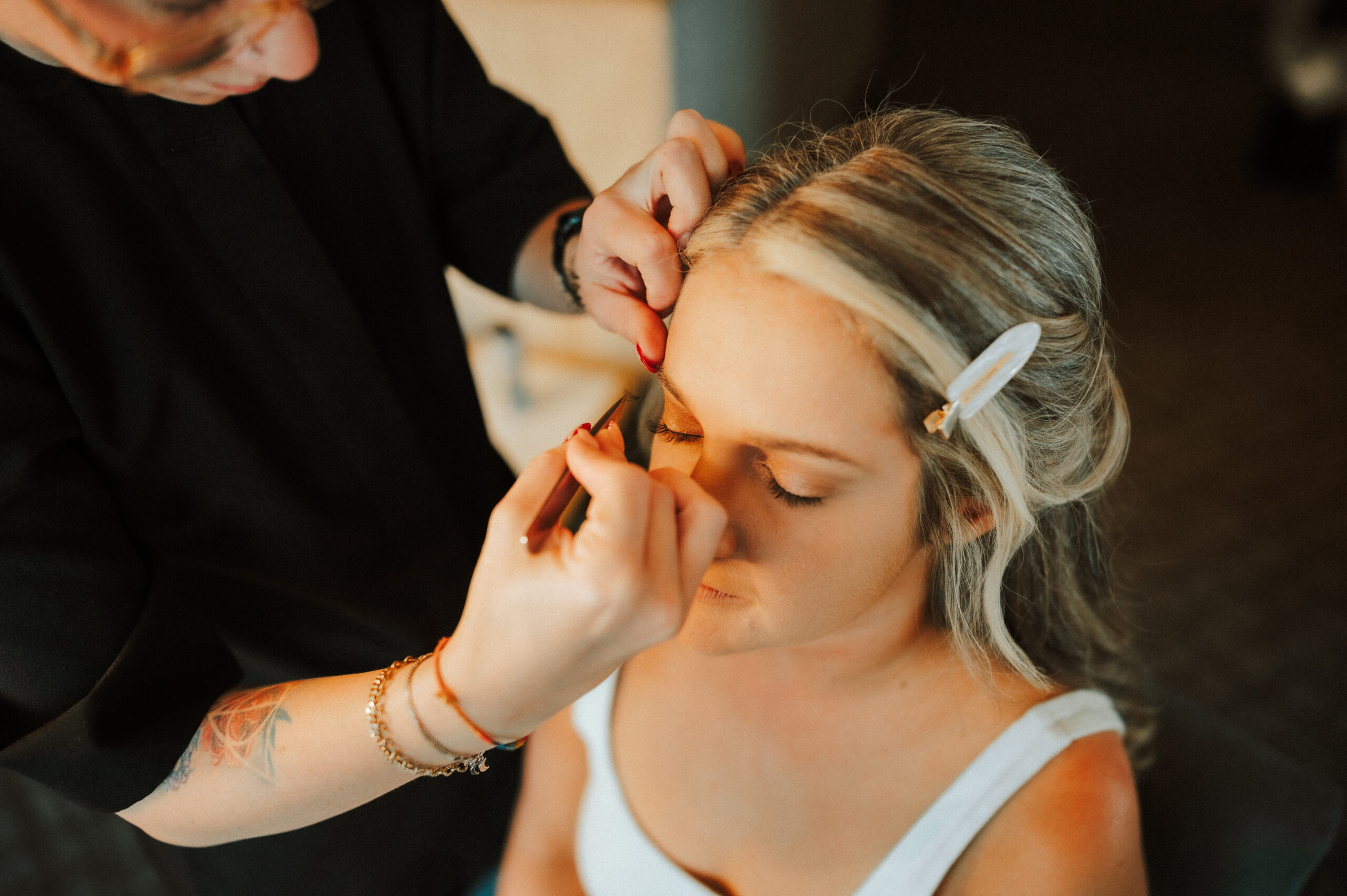 Bride receiving eyebrow shaping from a makeup artist, showcasing wedding hair and makeup done by the professionals at Kristy's Artistry Design Team.