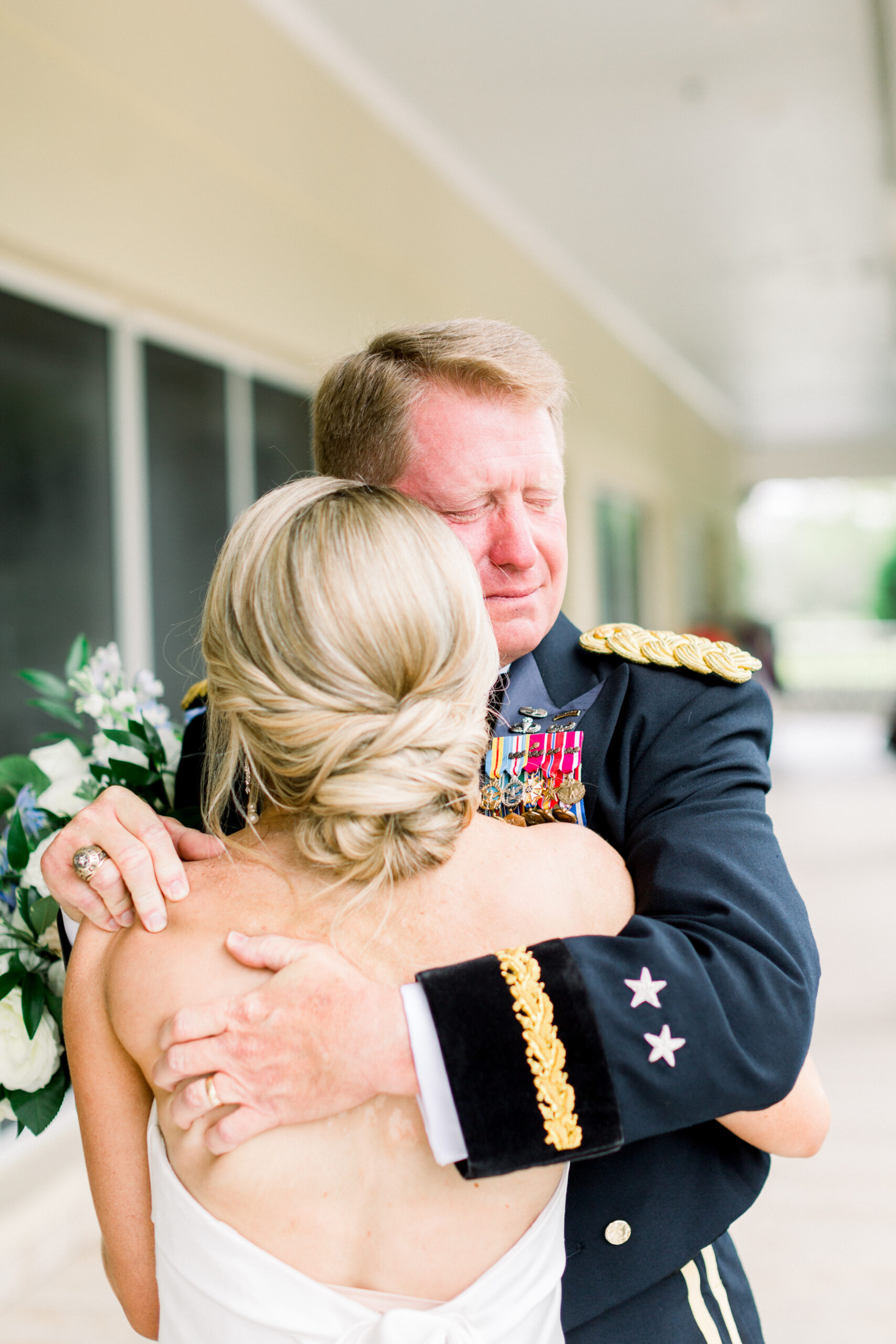 Bride with elegant updo and makeup by Kristy's Artistry Design Team, embracing her emotional military father pre-wedding.