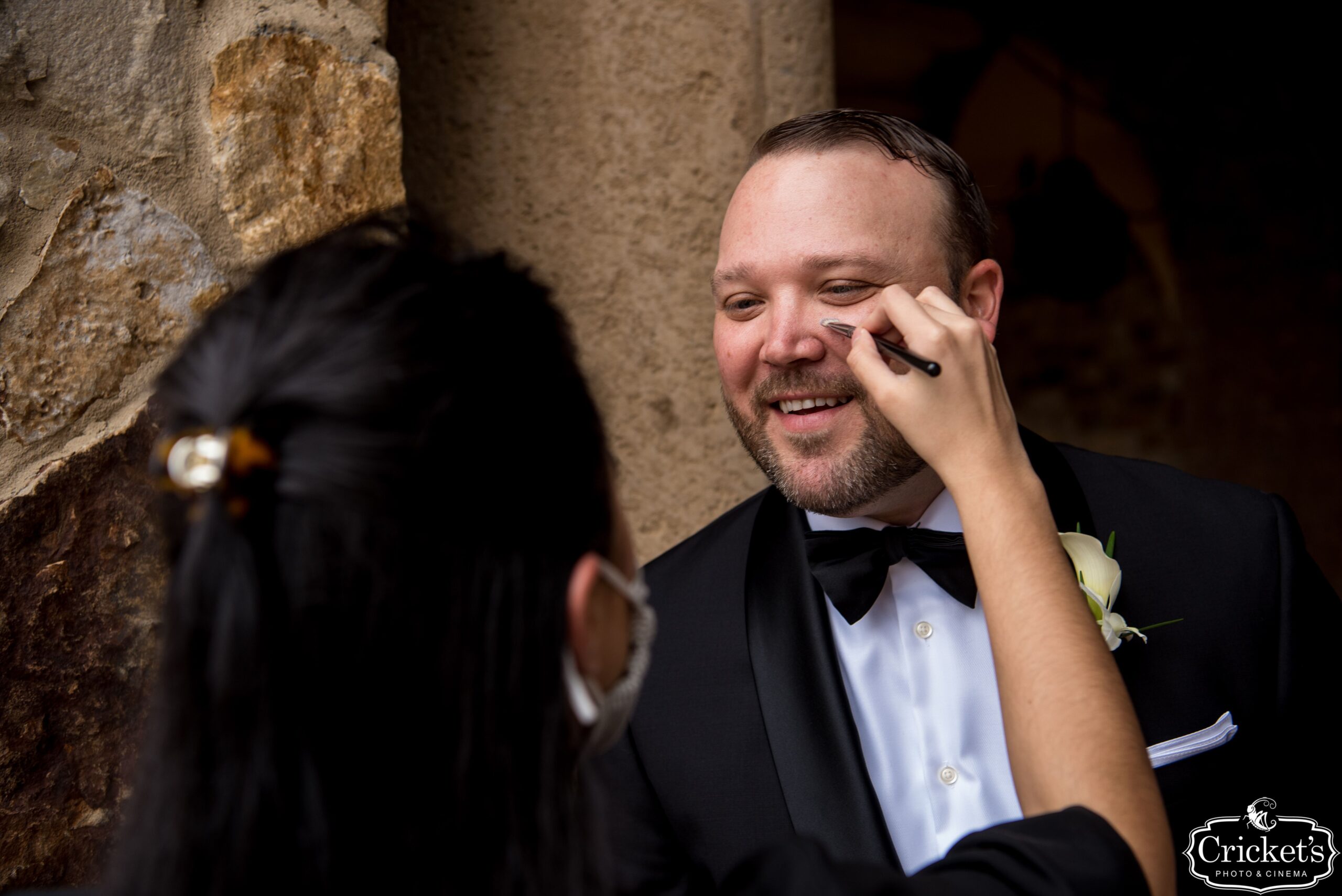 Groom getting makeup applied under his eye pre-wedding by an artist from Kristy's Artistry Design Team.