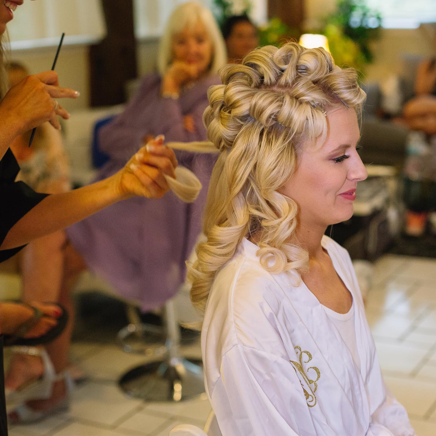 Bride with curlers in her hair being prepped by an artist from Kristy's Artistry Design Team.