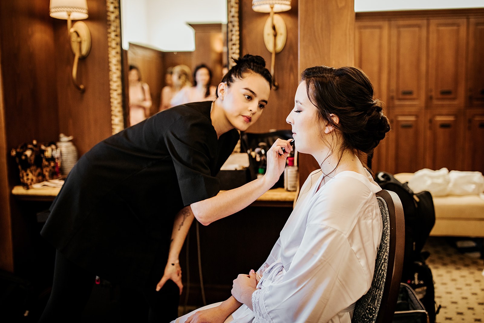 Makeup artist applying makeup to a bride in a bridal suite, from Kristy's Artistry Design Team.