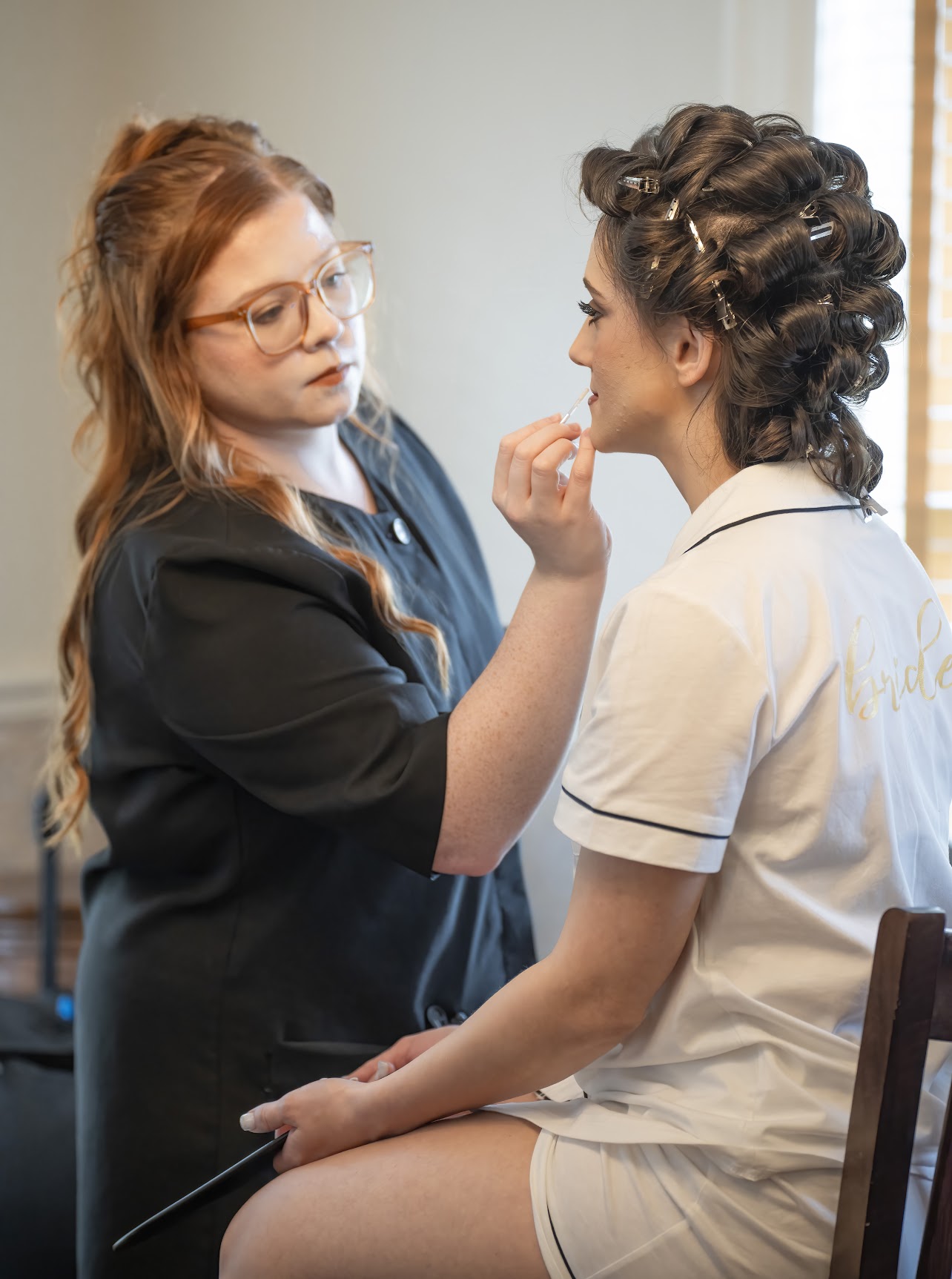 Professional makeup artist from Kristy’s Artistry Design Team applying lip balm with precision to the bride in the bridal suite.