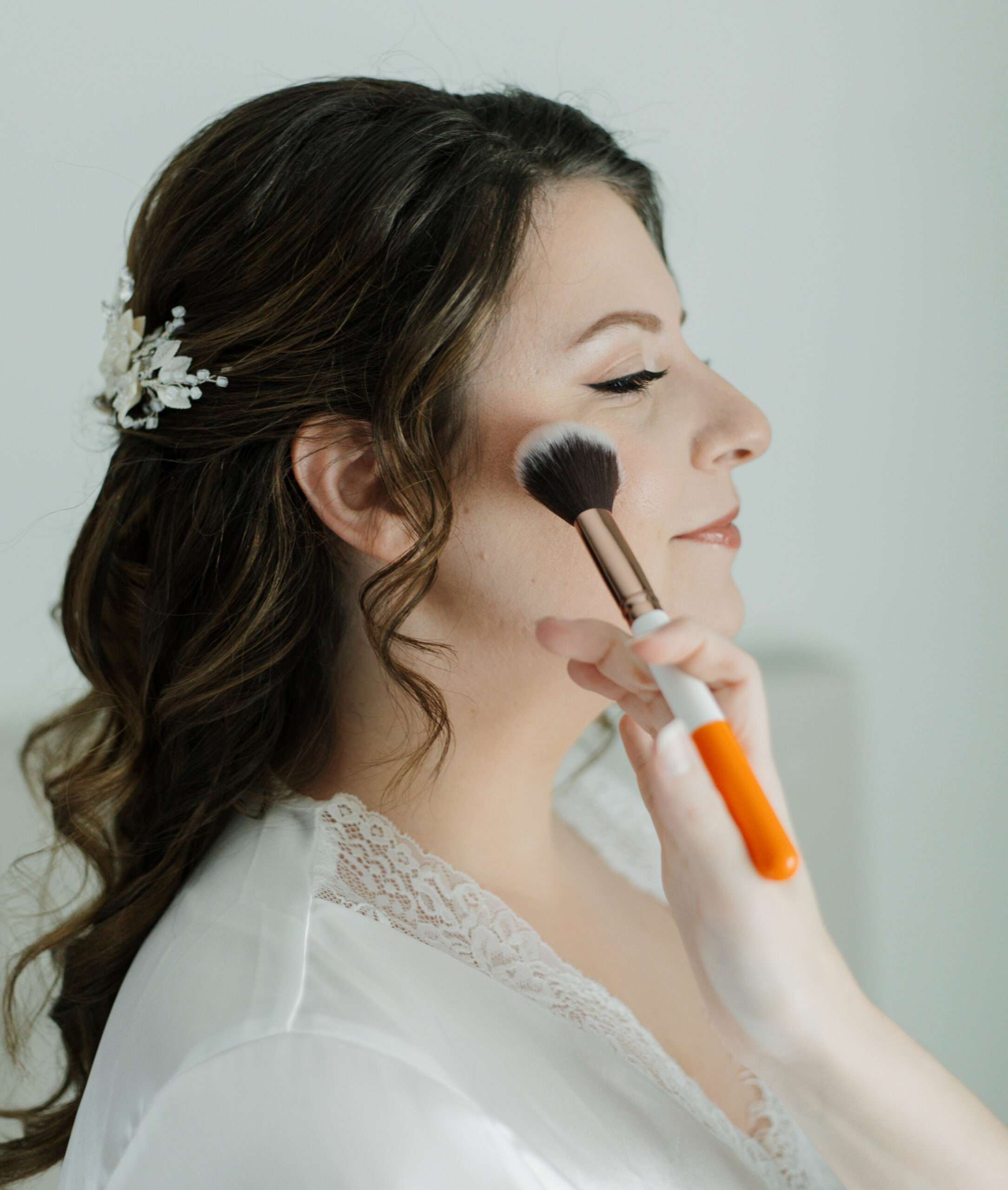 Bride receiving finishing touches as makeup artist touches up her blush.