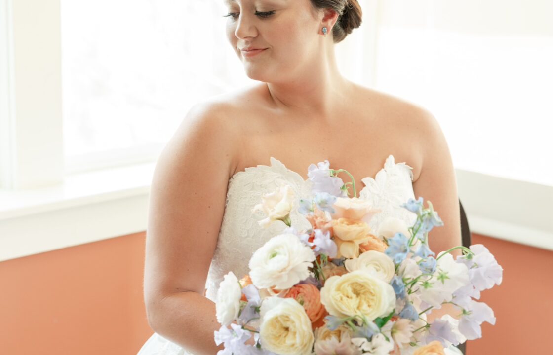 bride holding pastel floral bouquet with slicked back low bun wedding hairstyle