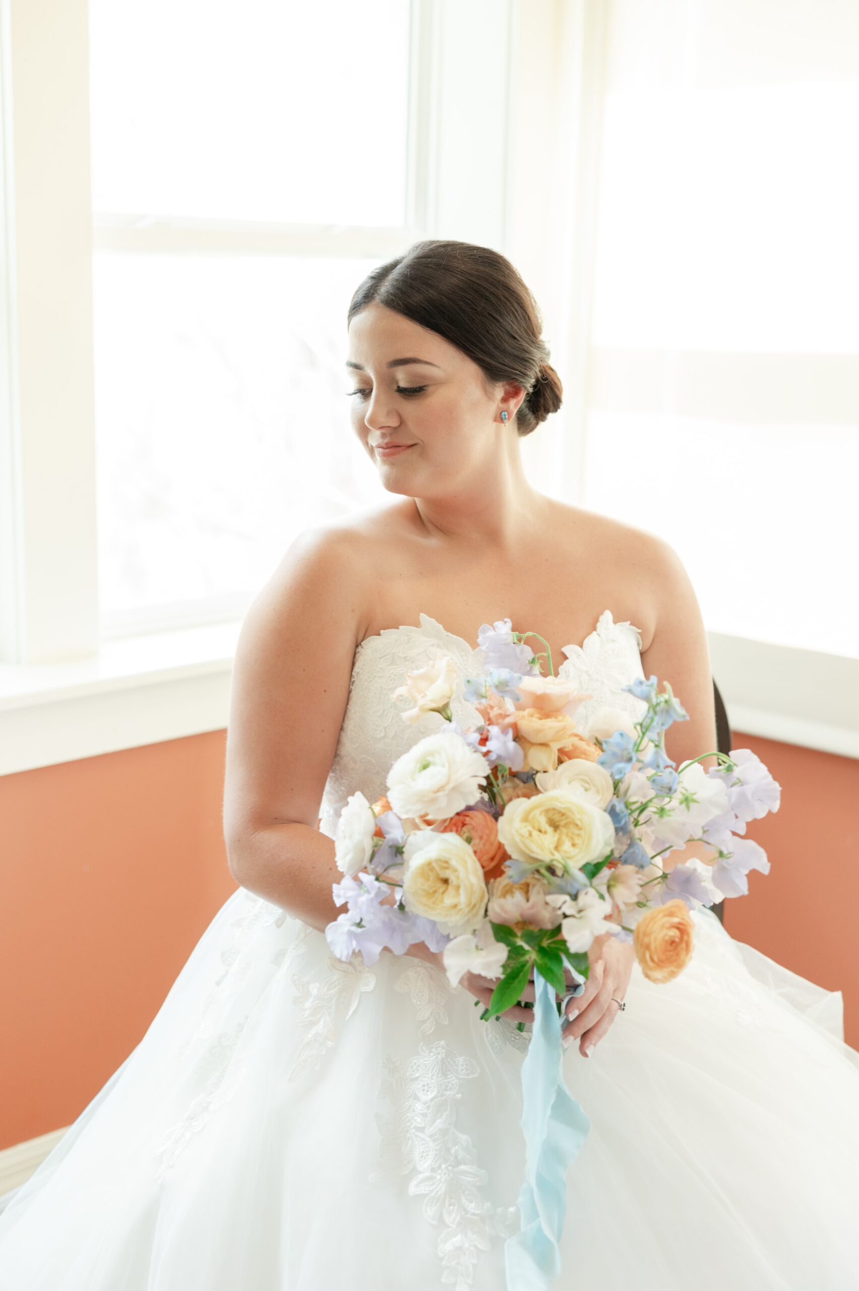 bride holding pastel floral bouquet with slicked back low bun wedding hairstyle