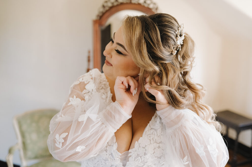 bride puts on earring after hair and makeup by Kristy's Artistry Design Team Fl