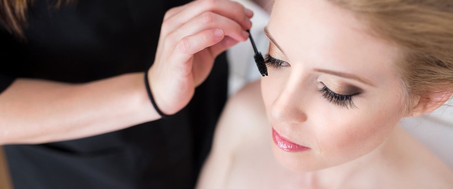 Woman having mascara applied by makeup artist.