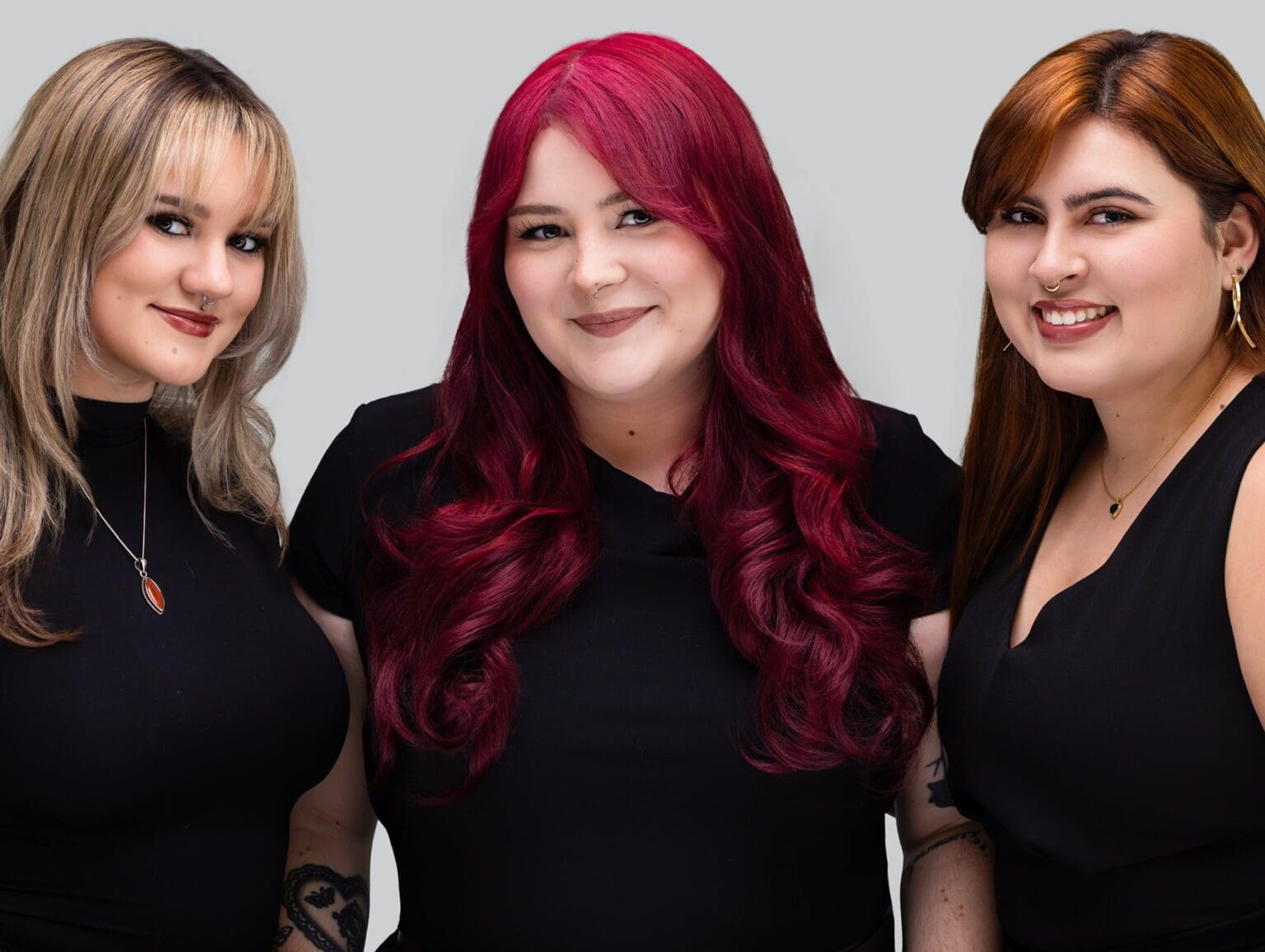 Three women smiling against a gray background.