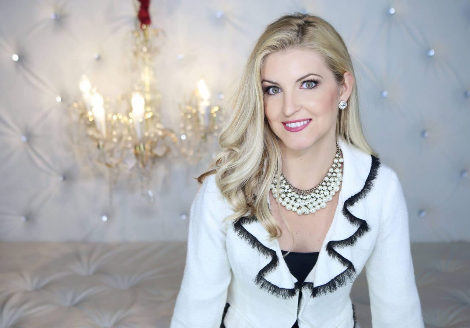 Smiling woman in elegant attire, chandelier background.
